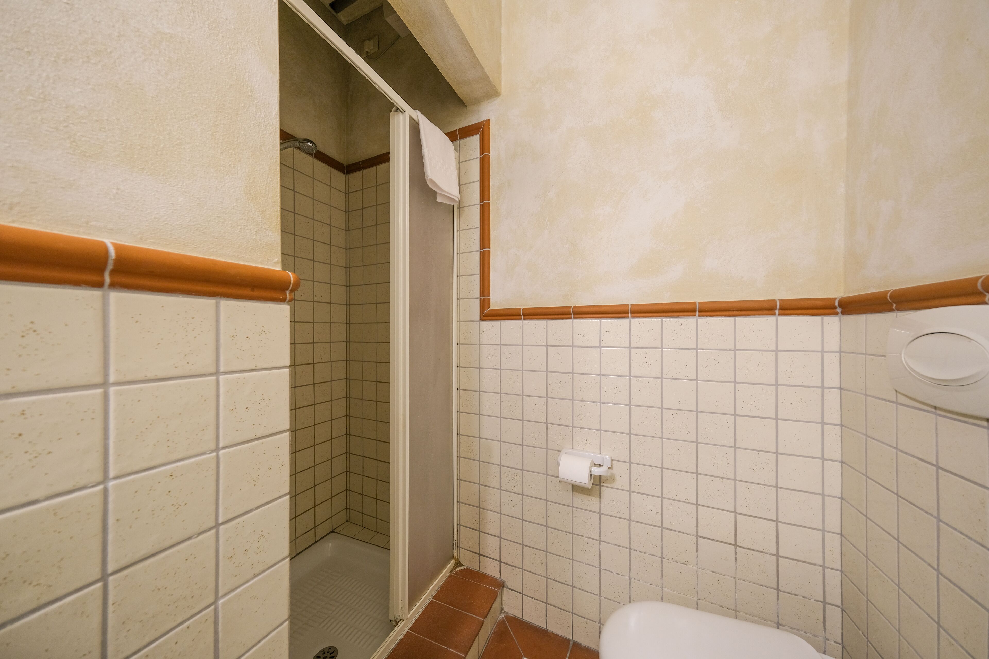 A bathroom with white tiled walls, a shower area, and a toilet.