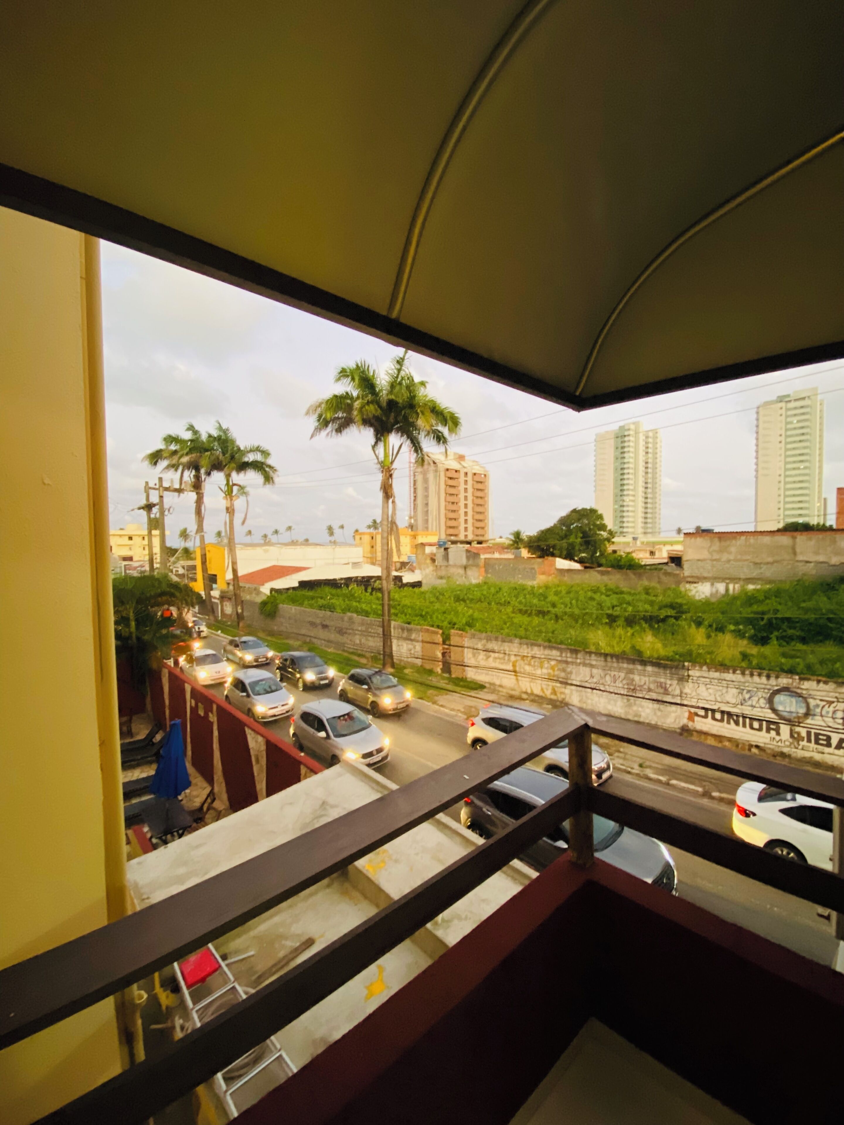 Un balcón con vista a una calle, coches, palmeras y edificios altos.
