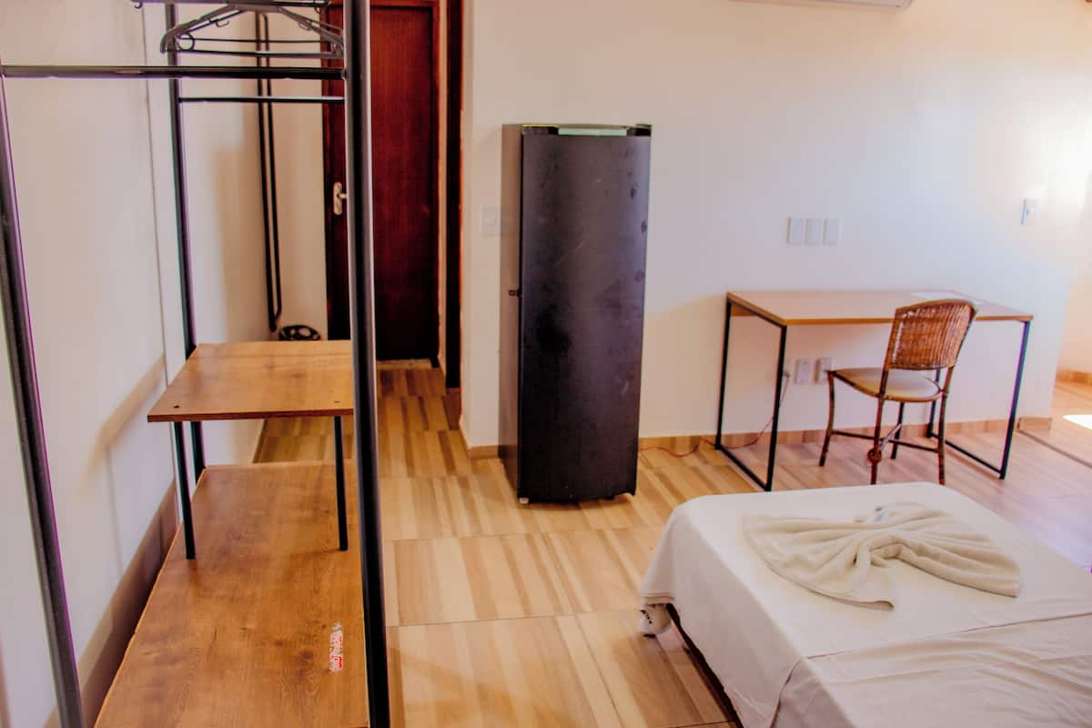 Una habitación con cama, escritorio, silla, armario y perchero.