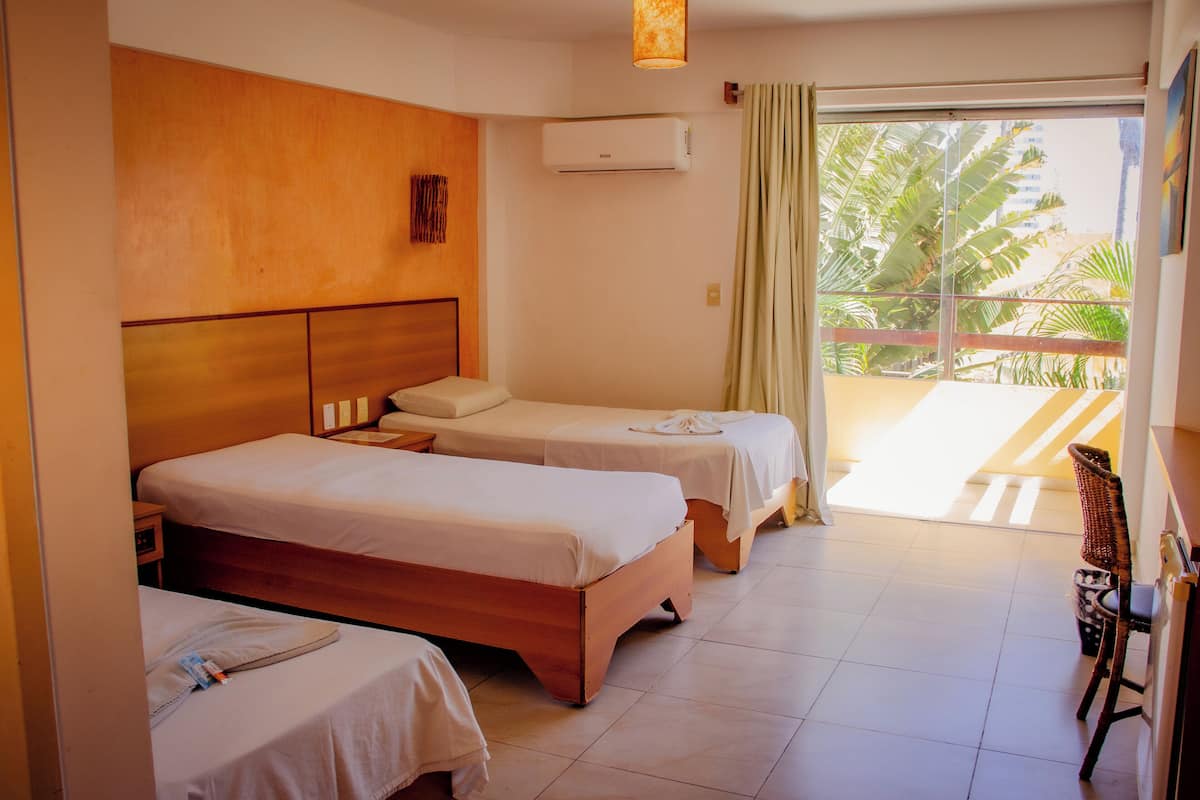 Habitación de hotel con dos camas, cabecera de madera, ventana con cortinas y vistas a palmeras.
