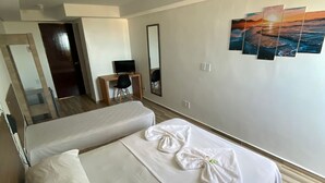 Habitación de hotel con una cama grande, un escritorio con silla, un espejo y un cuadro de atardecer en la pared.