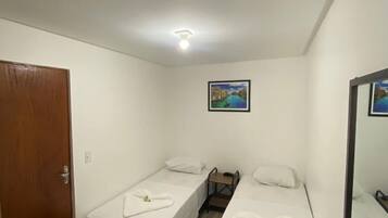 A small, clean room with two single beds, a wooden door, a desk with a chair, and a painting on the wall.