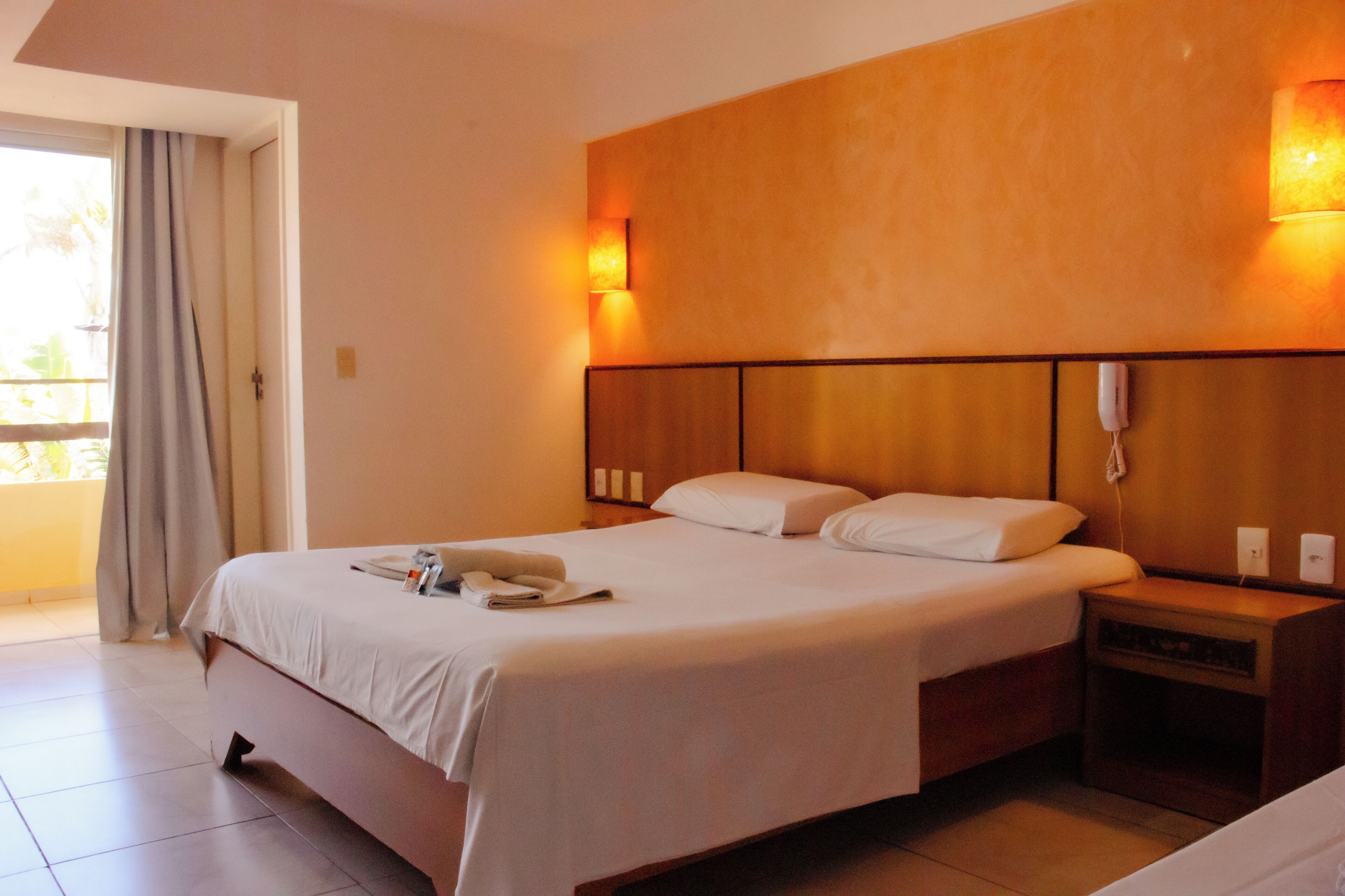 Ein Hotelzimmer mit einem großen Bett, Nachttischen, einem Telefon und Blick ins Freie.