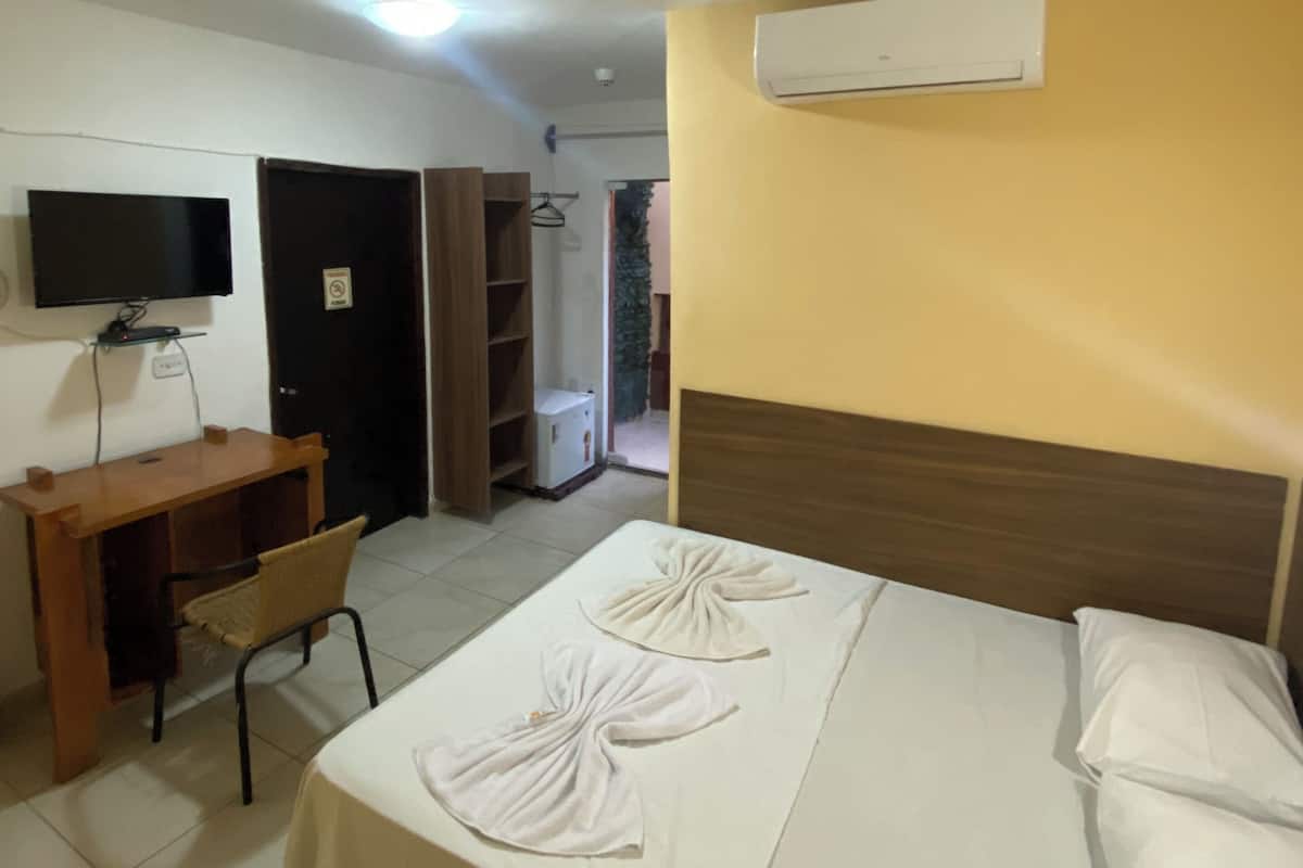 Una habitación de hotel con una cama, un escritorio, una silla, aire acondicionado y una televisión.