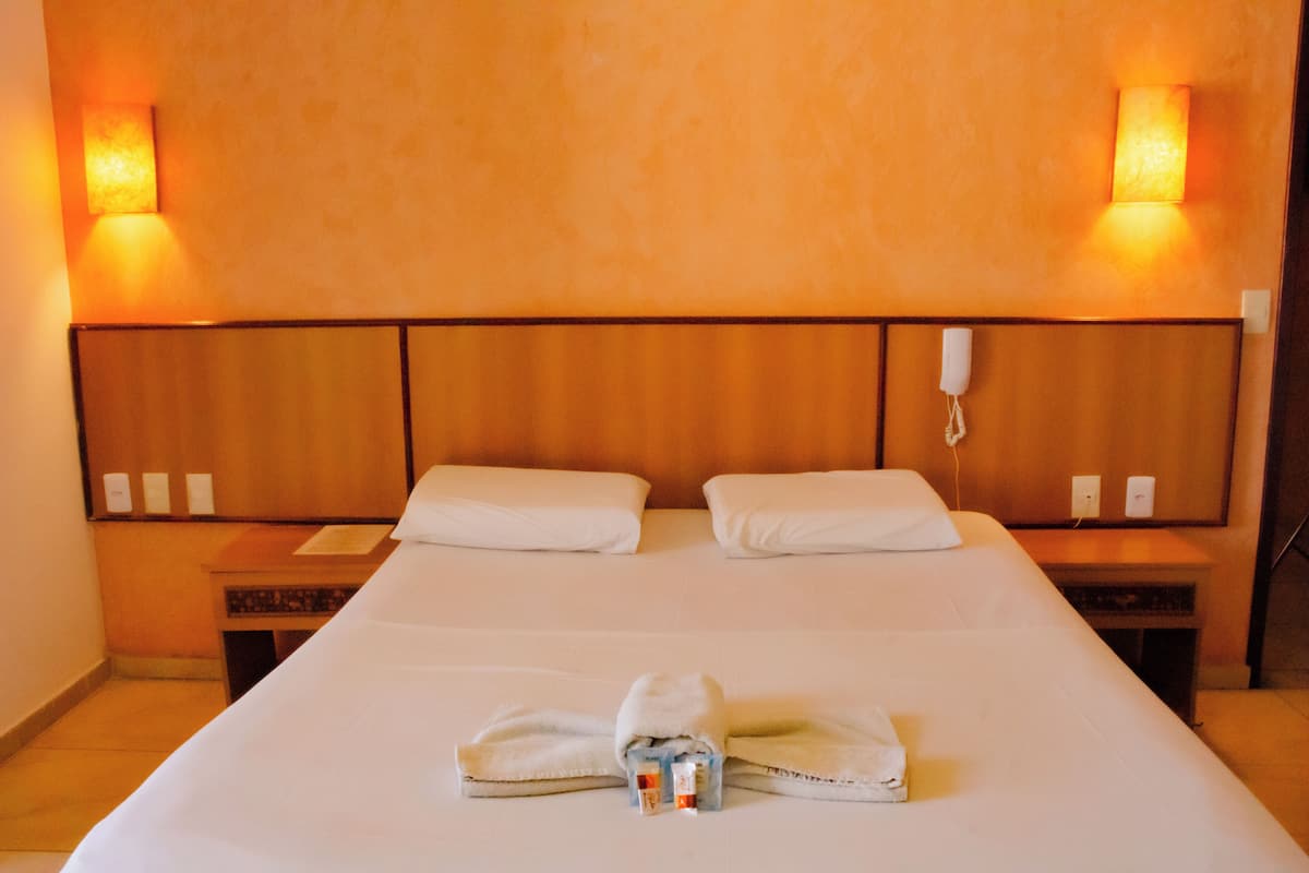 Habitación de hotel con una cama grande, dos mesitas de noche, un teléfono en la pared y dos apliques.