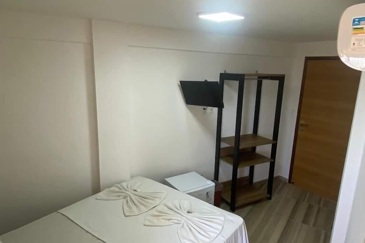Una habitación pequeña y ordenada, con una cama individual, un estante de madera y una puerta.