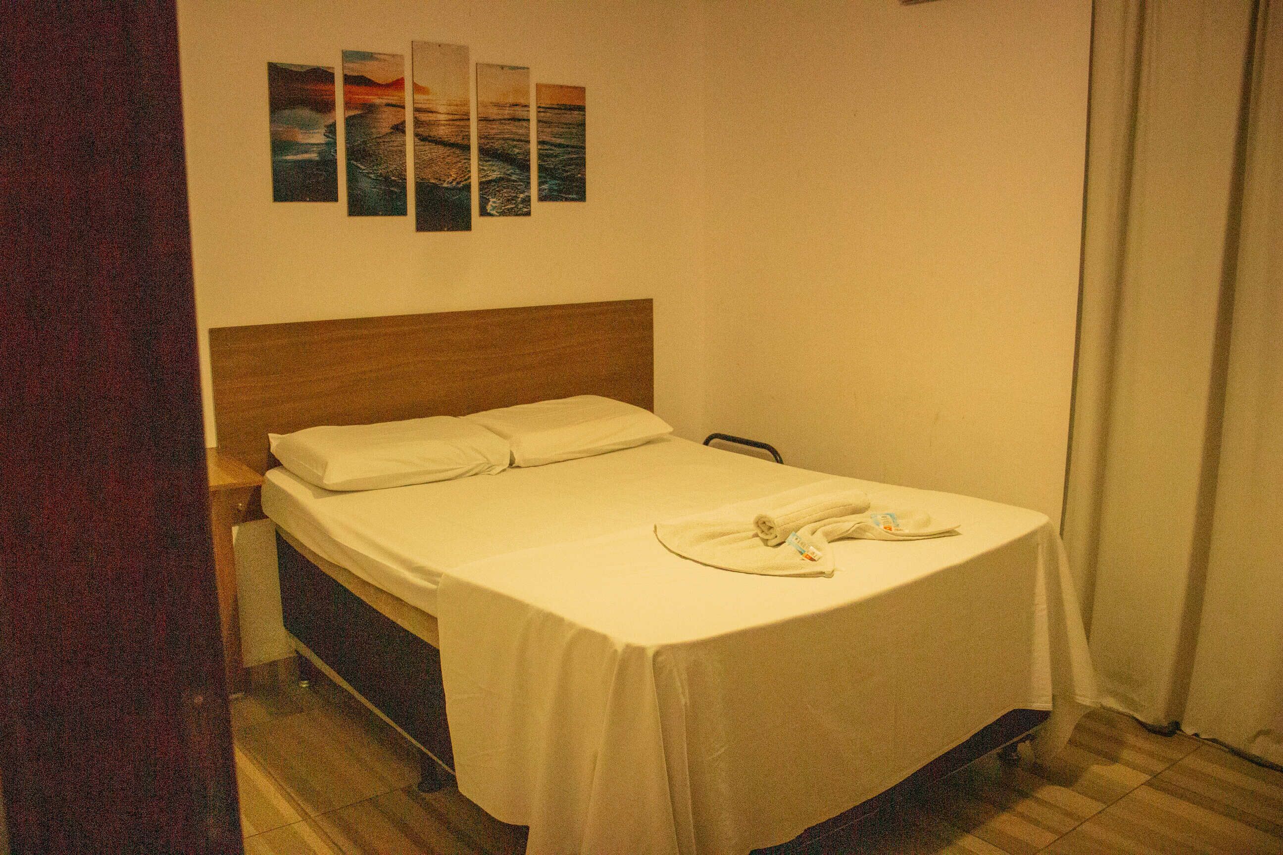 Una cama individual con cabecera de madera, una colcha blanca y un juego de toallas blancas sobre la cama.