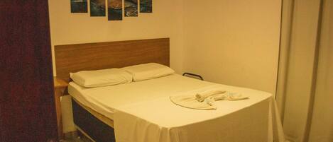 Una cama individual con cabecera de madera, una colcha blanca y un juego de toallas blancas sobre la cama.
