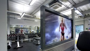 Une salle de sport équipée de matériel d’exercice, dotée d’un grand miroir et d’un écran de télévision diffusant une image.