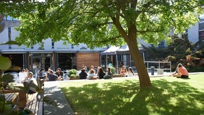 Un espace extérieur aménagé avec des tables et des chaises, entouré de verdure et avec un bâtiment en arrière-plan.
