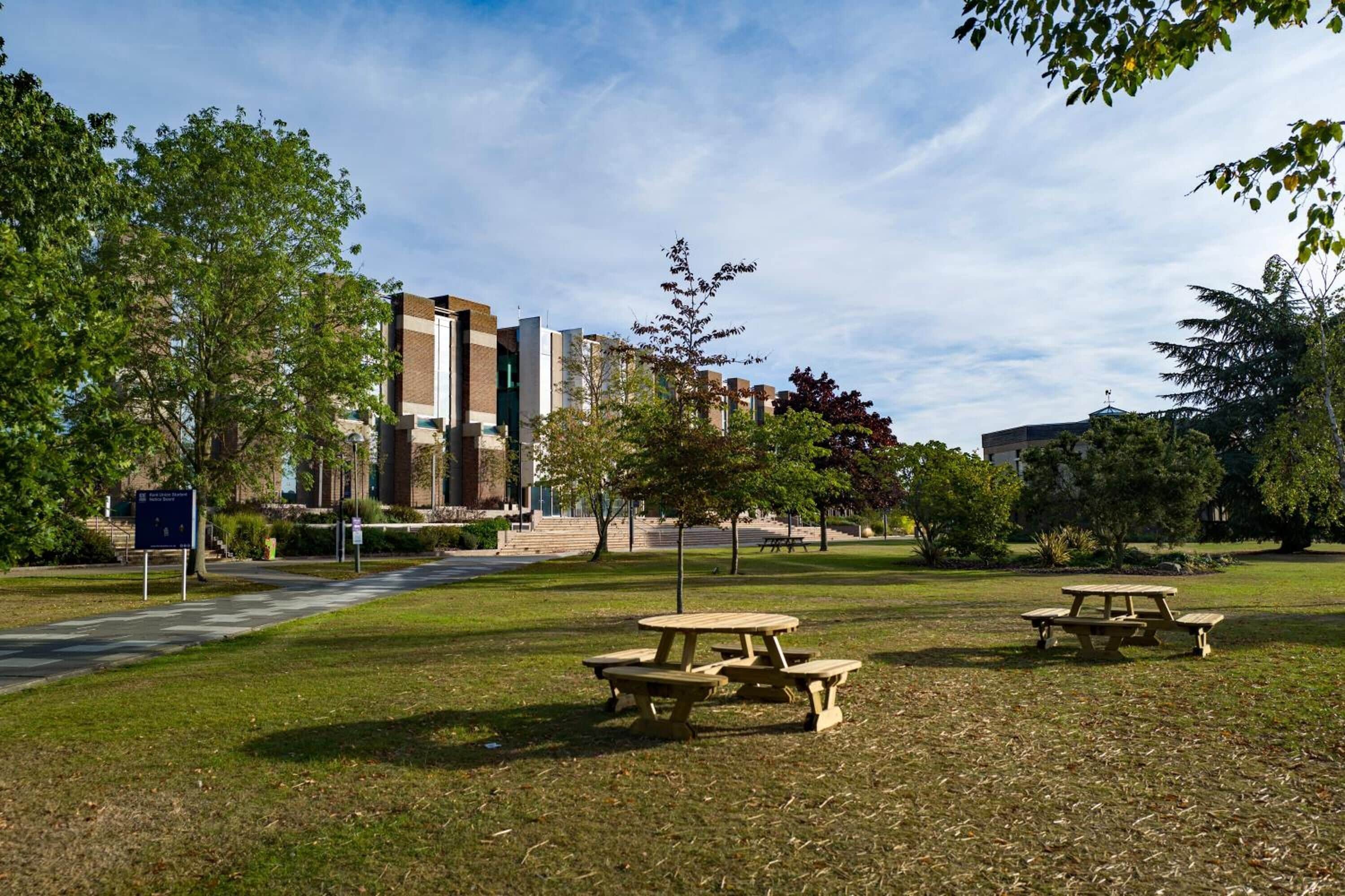 A grassy area with picnic tables and a pathway leading to a building with a brick facade.