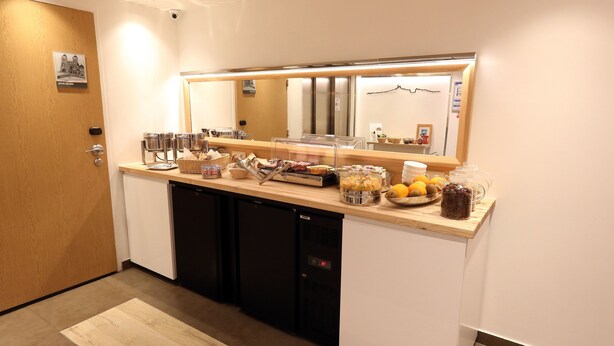 A kitchen area with a wooden door, a refrigerator, a sink, and a counter with various food items and containers. - Best Western Hotel du Mucem (Marseille)