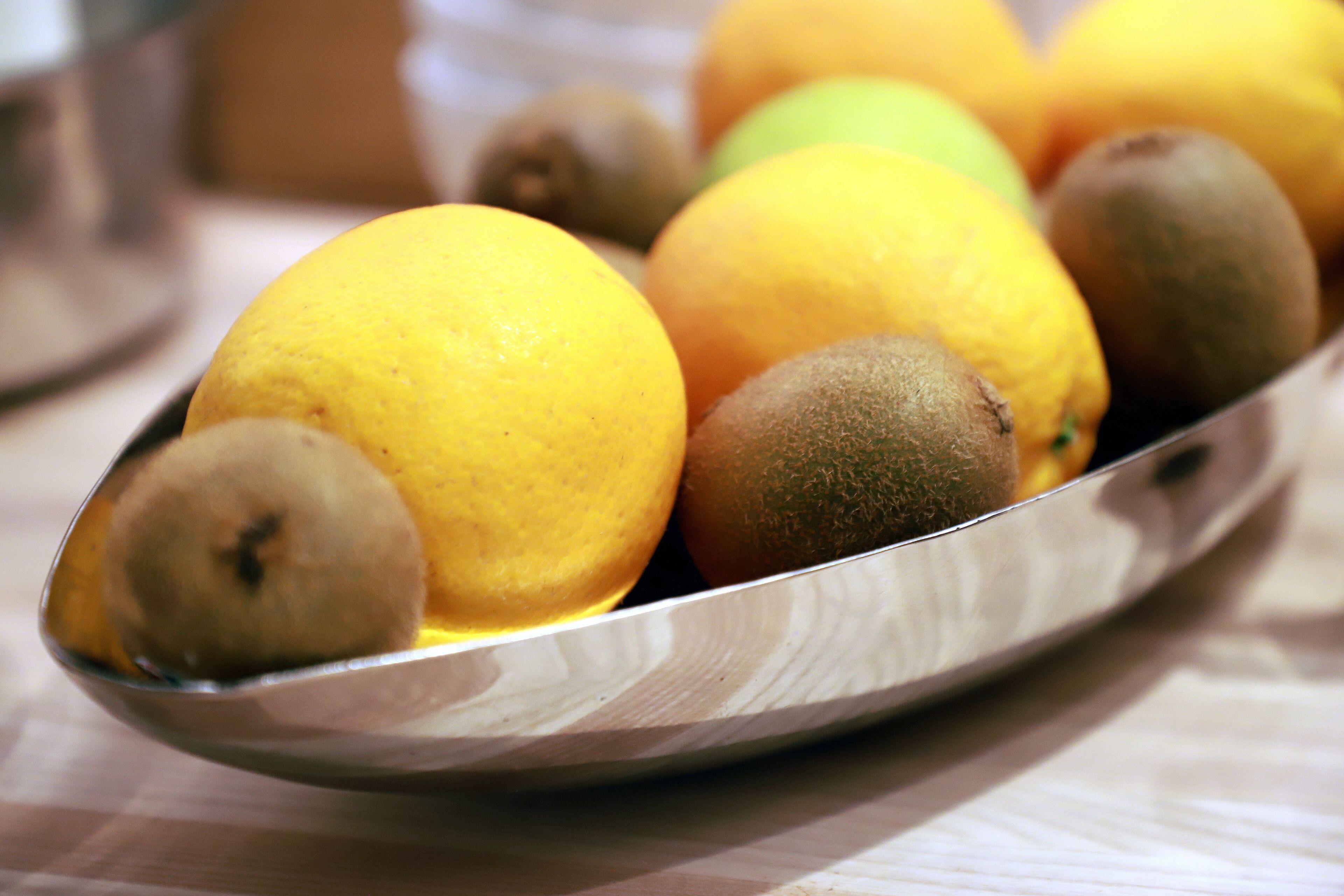 A metal tray with oranges and kiwis on a table.