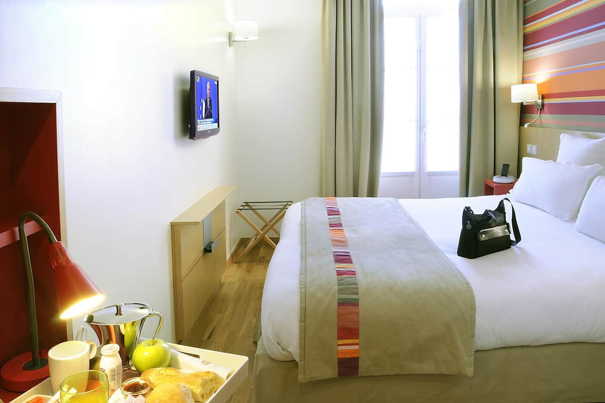 Een hotelkamer met een bed, een bureau met lamp, een televisie en een raam met gordijnen.