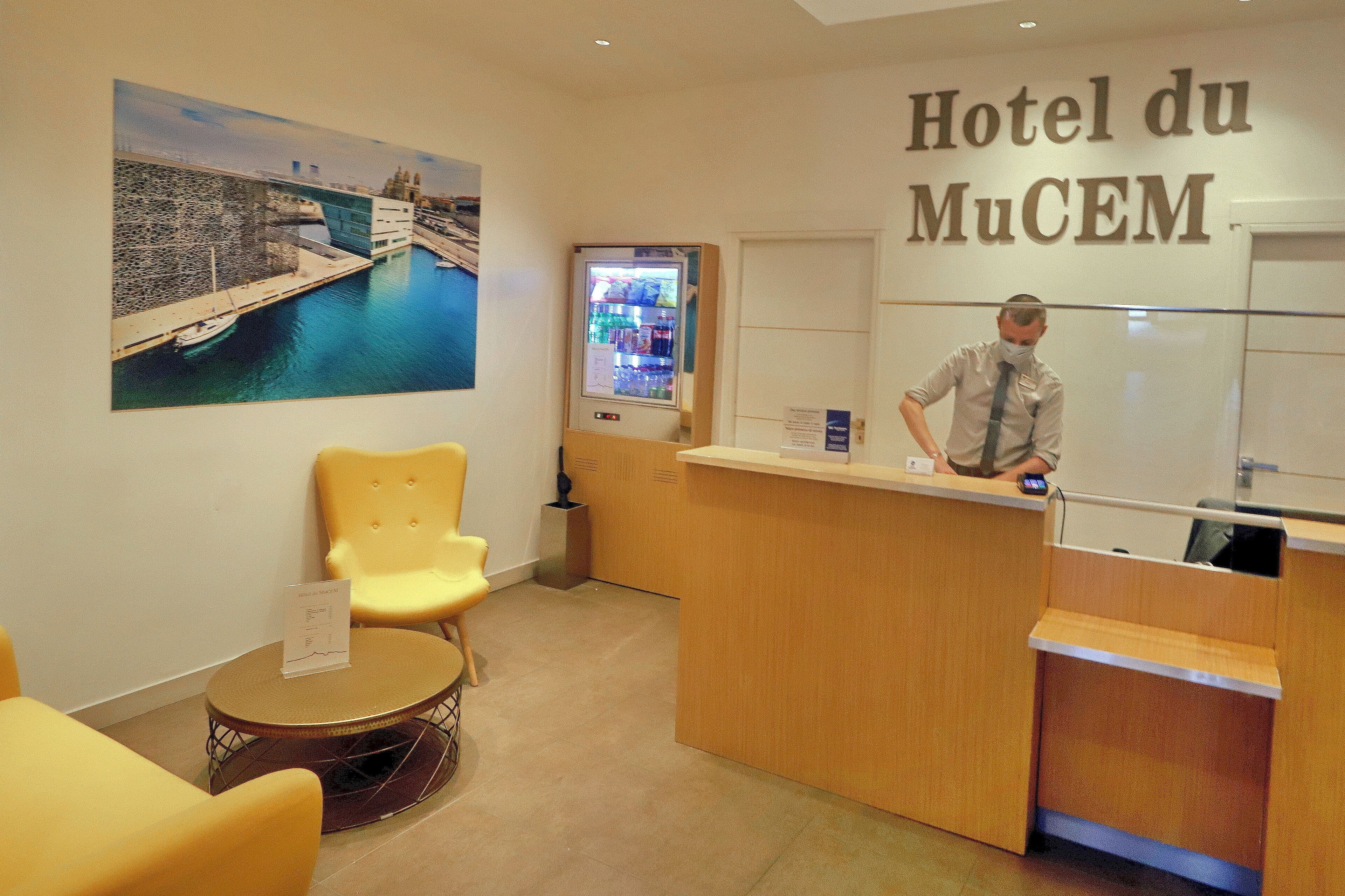 A hotel reception area with a counter, a seating area with yellow chairs, and a large painting of a bridge over water.