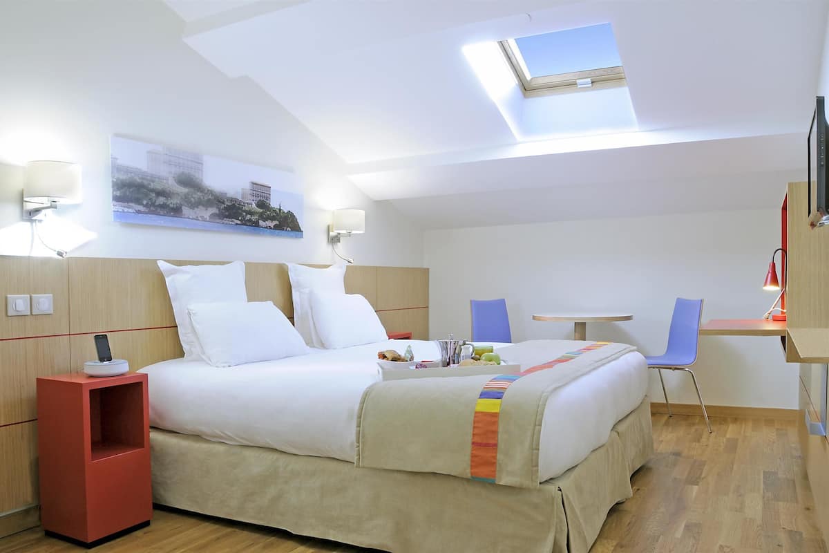 Een hotelkamer met een bed, een bureau, een stoel, een televisie en een schilderij aan de muur.