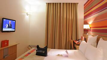 Quarto de hotel com uma cama, televisão, escrivaninha e uma cadeira.