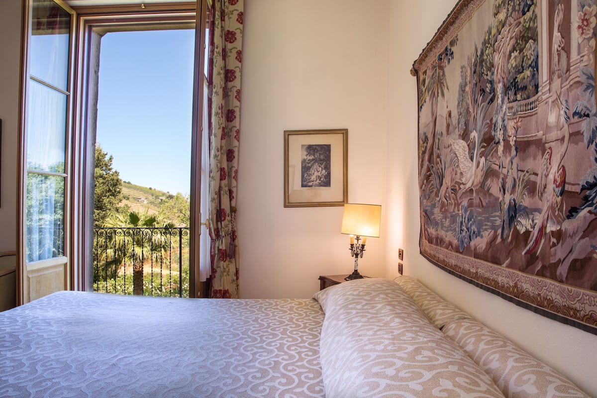 Une chambre d’hôtel avec un grand lit, une vue sur un balcon, un tableau au mur et une lampe sur la table de chevet.