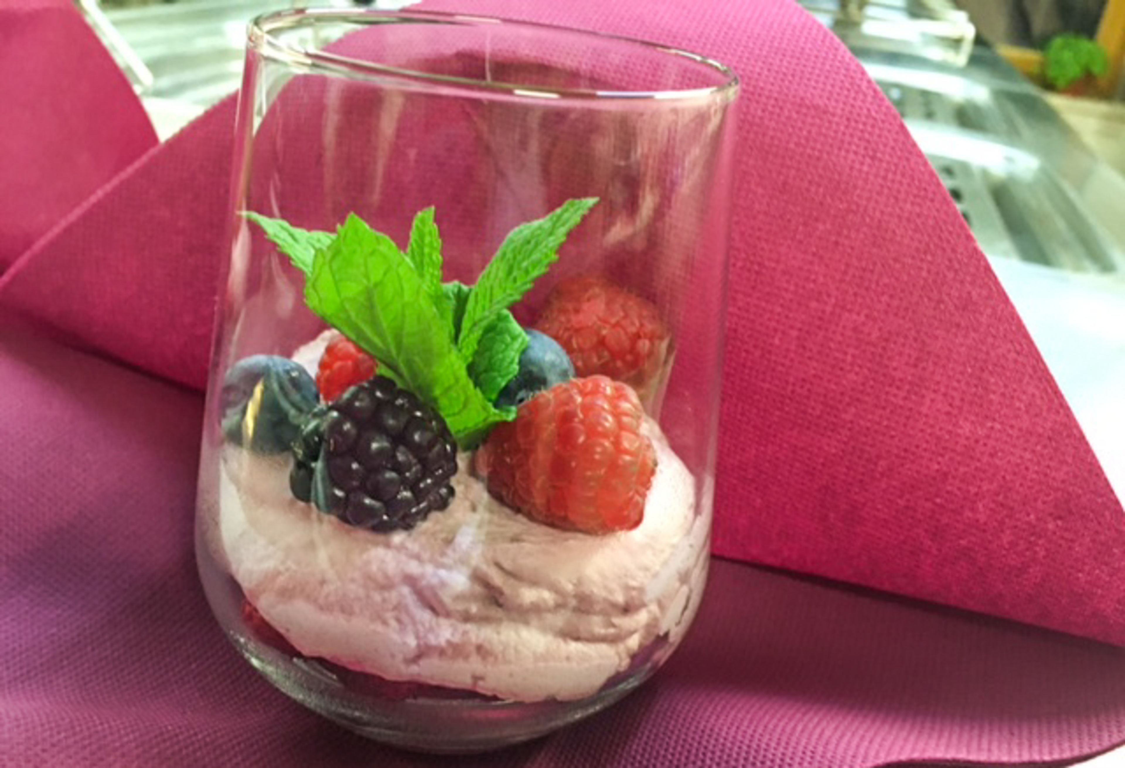 Un dessert in un bicchiere trasparente con frutti di bosco e foglie di menta.