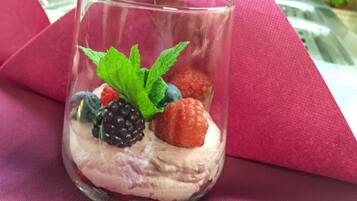 Un dessert in un bicchiere trasparente con frutti di bosco e foglie di menta.