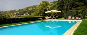 Ein Swimmingpool mit Hängematte und Liegestühlen, umgeben von Grünflächen und Hügeln.