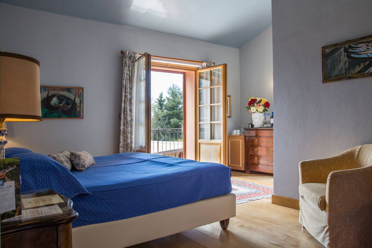 Une chambre à coucher avec un lit, une commode, une chaise, une fenêtre et un tableau accroché au mur.