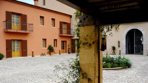 A courtyard with cobblestone flooring, a building with balconies and wooden shutters, and potted plants. - Agrirelais Baglio di Pianetto (Santa Cristina Gela)