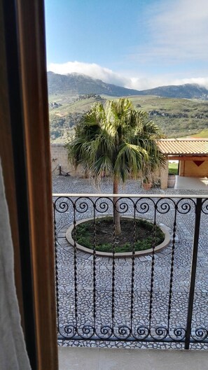 A balcony with a palm tree, a stone-tiled floor, and a view of mountains. - Agrirelais Baglio di Pianetto (Santa Cristina Gela)