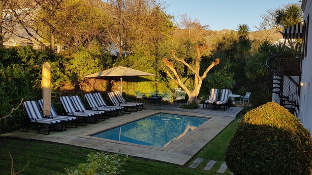 A pool area with lounge chairs and a table, surrounded by greenery and trees. - Maison Chablis (Franschhoek)