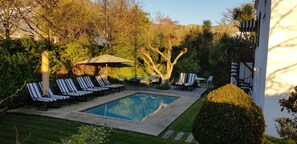 A pool area with lounge chairs and a table, surrounded by greenery and trees. - Maison Chablis (Franschhoek)