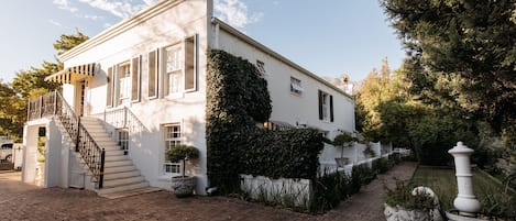 A white building with a brick pathway, a staircase, and a garden area with potted plants.