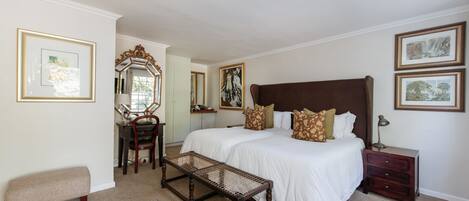Een slaapkamer met een groot bed, een houten bankje, een bureau en een dressoir.