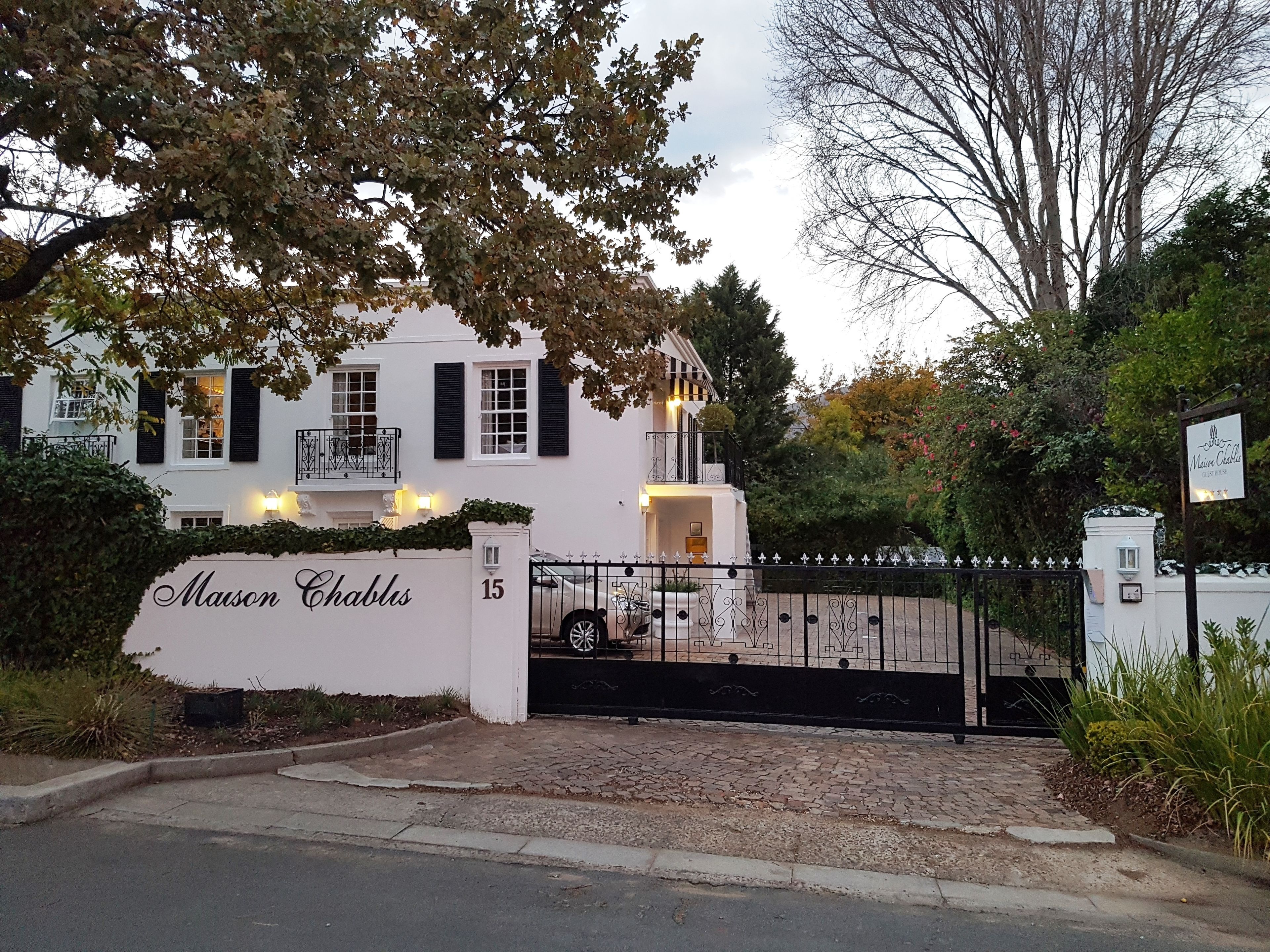 A white building with black shutters, a gated entrance, and a sign reading "Maison Chablis."