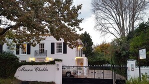 A white building with black shutters, a gated entrance, and a sign reading "Maison Chablis." - Maison Chablis (Franschhoek)