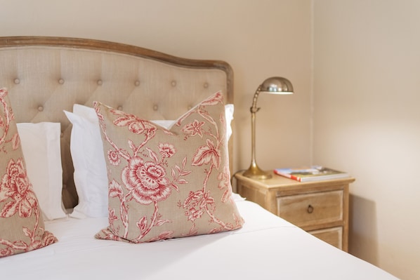A bed with floral-patterned pillows, a wooden headboard, and a bedside table with a lamp and a book. - Maison Chablis (Franschhoek)