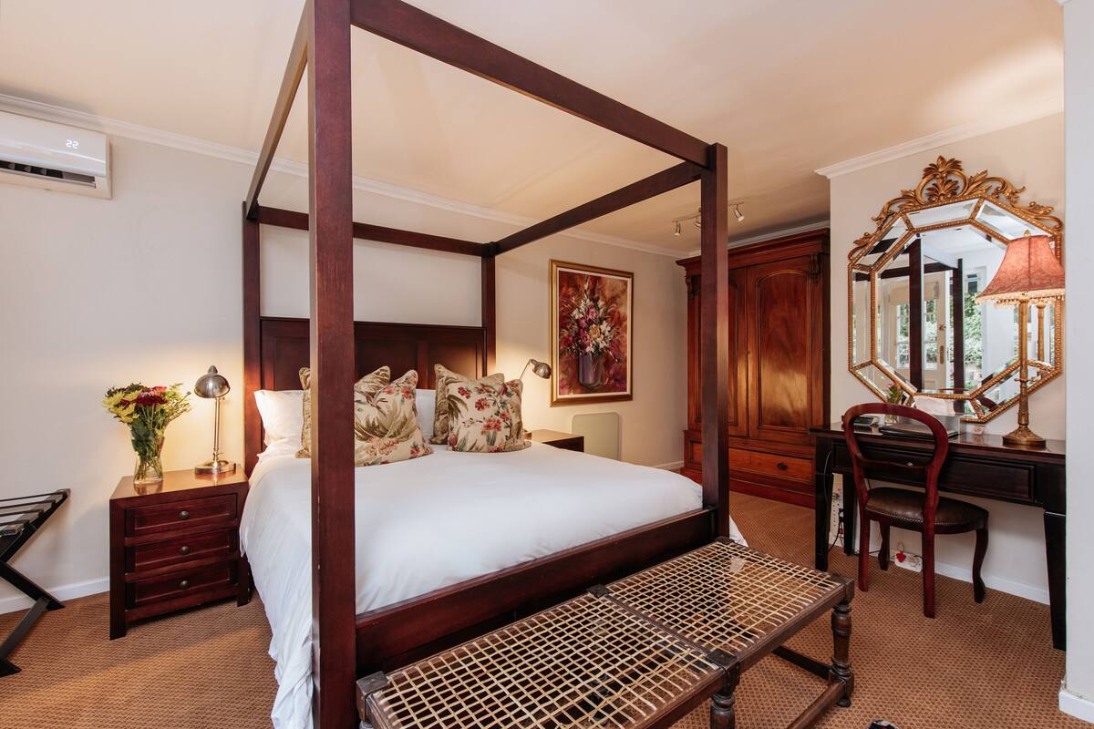 Un lit à baldaquin avec un cadre en bois, un bureau avec un miroir et une chaise.