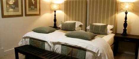 Un dormitorio ordenado con una cama, dos mesitas de noche, un banco y dos lámparas de pared.