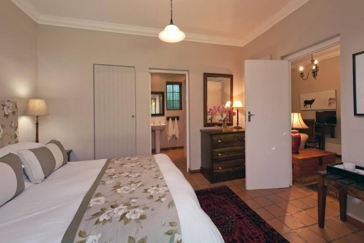 A bedroom with a bed, a dresser, a mirror, a lamp, and a door leading to another room.