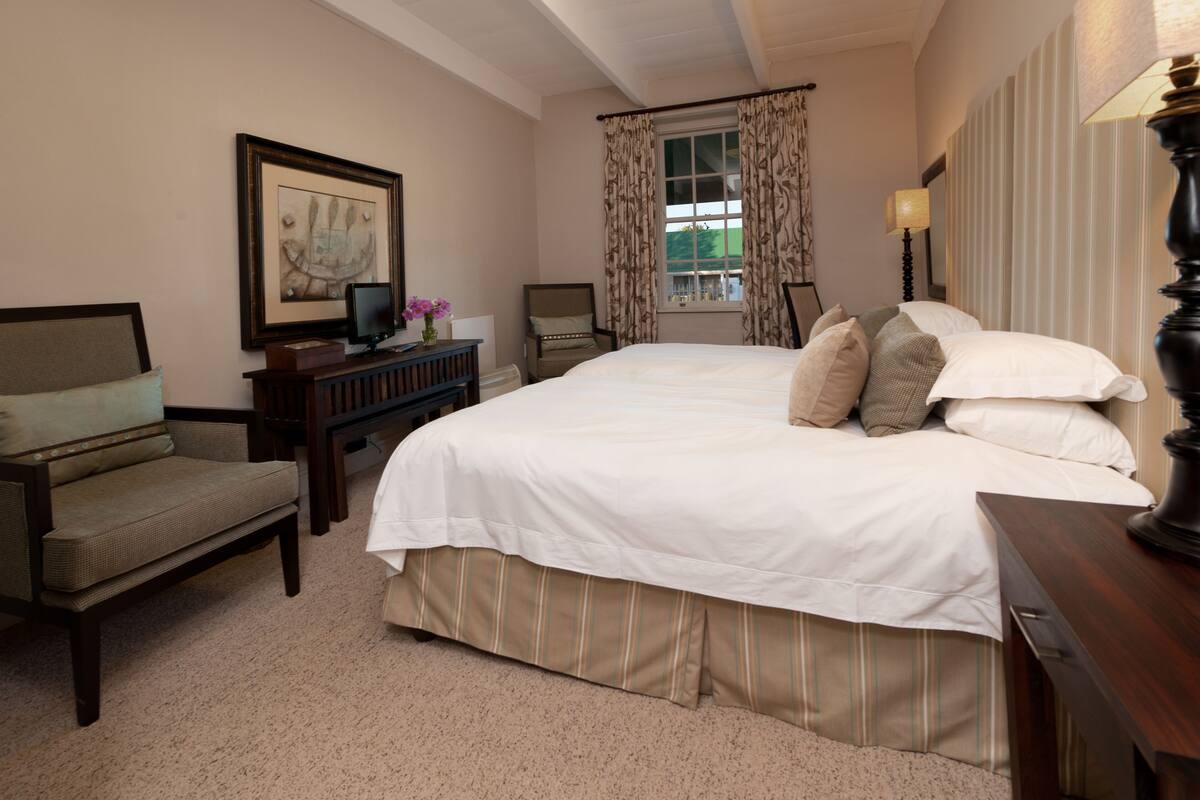 A hotel room with a large bed, a desk with a computer, a chair, and a window with curtains.