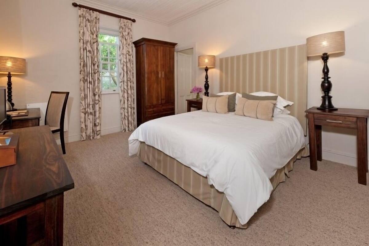 A neatly arranged bedroom with a large bed, a wooden wardrobe, a desk, and a chair.