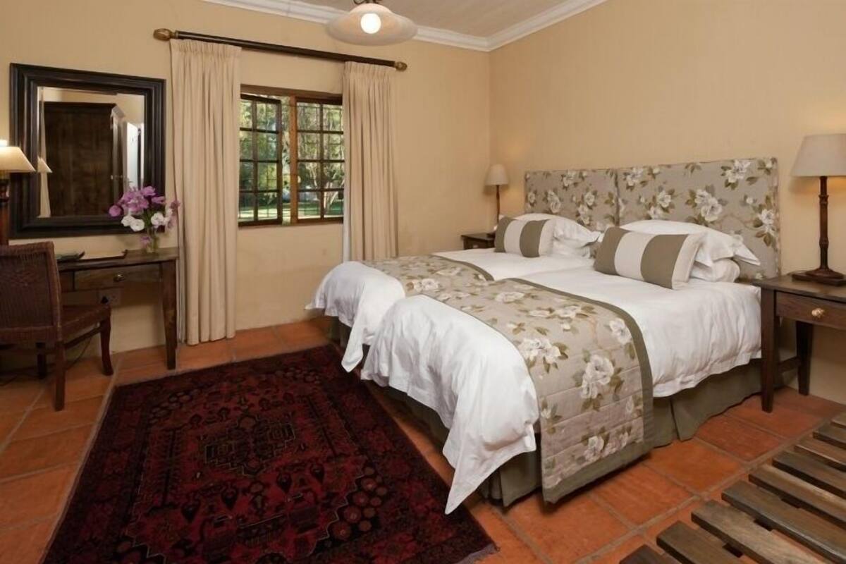 A bedroom with two beds, a desk, a chair, a large mirror, and a window with curtains.
