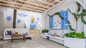 Un espacio al aire libre acogedor con sofá y mesa, una escalera y elementos decorativos como un jarrón azul y faroles en la pared.