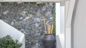Una escalera con un muro de piedra, una olla negra con ramas y plantas verdes.