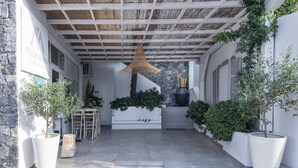 Una villa moderna con fachada de piedra, un porche cubierto con techo de mimbre y grandes macetas con plantas.