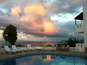 A poolside area with lounge chairs and a view of the sea under a cloudy sky. - Thalia Apartments (Malevizi)