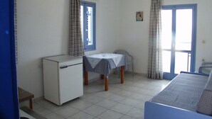 A small, simple room with a kitchenette, a table with a checkered tablecloth, and two windows with curtains. - Thalia Apartments (Malevizi)
