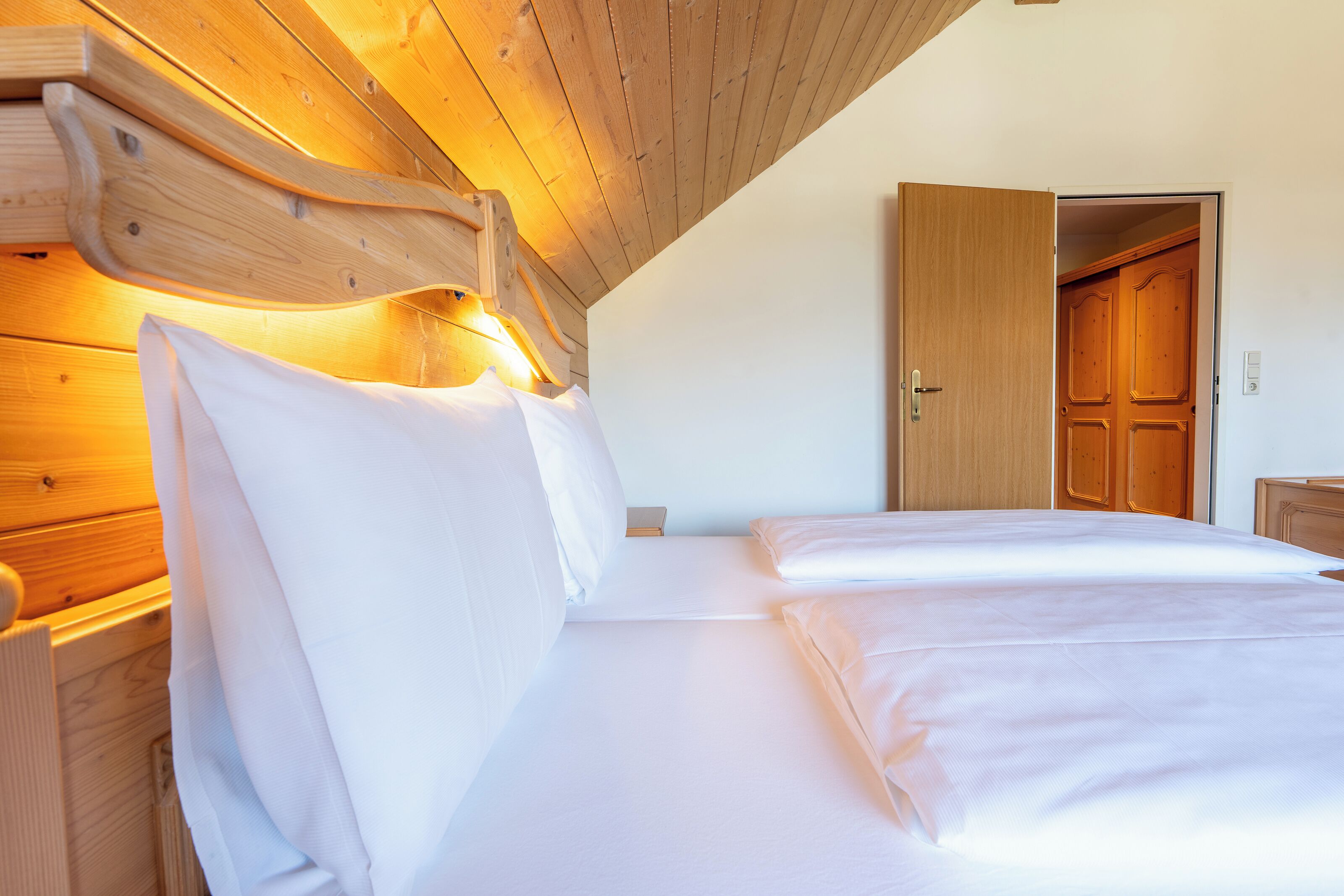 A bedroom with a wooden headboard, a bed with white linens, and a wooden door in the background.