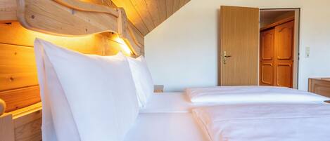 A bedroom with a wooden headboard, a bed with white linens, and a wooden door in the background.
