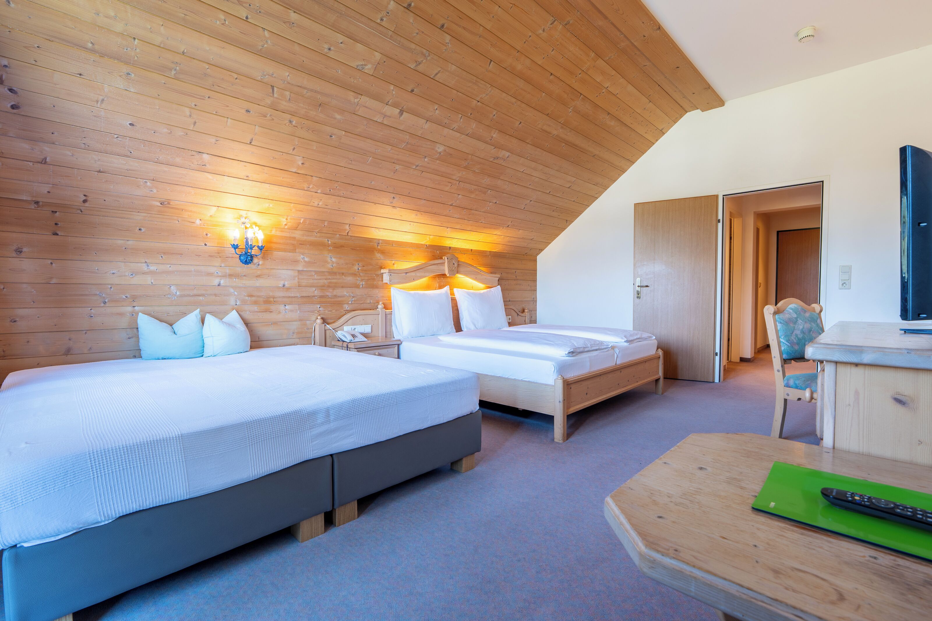 A bedroom with two beds, a wooden ceiling, a desk, and a chair.