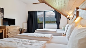 Habitación de hotel con dos camas, televisión, cómoda y vistas a montañas a través de un ventanal grande.